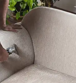Professional upholstery cleaner deep-cleaning a fabric sofa with a handheld extraction tool and hose Pittsburgh, PA.