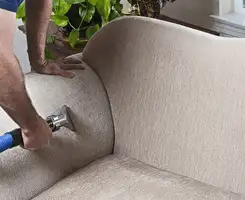 Professional upholstery cleaner deep-cleaning a fabric sofa with a handheld extraction tool and hose in Pittsburgh, PA.